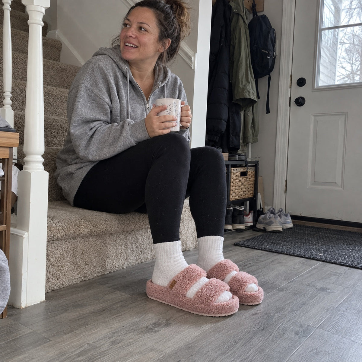 Woman sitting on her entryway stairs with a mug, wearing Fuzzy slides in Dusty Rose with white socks