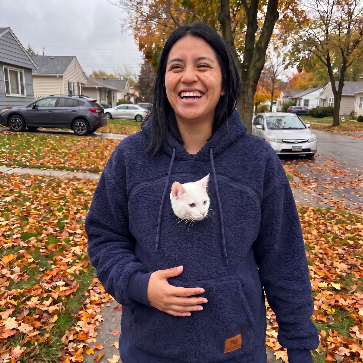Woman wearing the Meowdie cat pocket hoodie in Navy on a fall street, white cat peeking out
