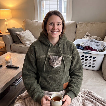Woman relaxing on her couch at home in the Meowdie cat pocket hoodie in Green, cat snuggled in the pouch